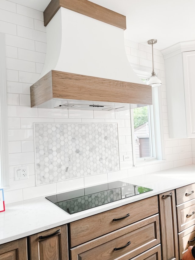 kitchen featuring backsplash, black electric stovetop, hanging light fixtures, and custom range hood