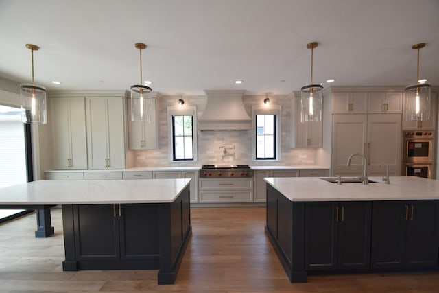 kitchen with light stone countertops, wall chimney exhaust hood, sink, hanging light fixtures, and a large island