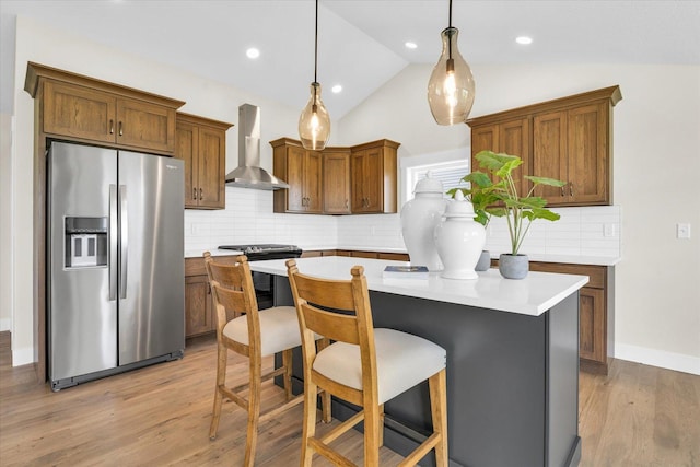 kitchen featuring pendant lighting, a center island, lofted ceiling, wall chimney range hood, and appliances with stainless steel finishes