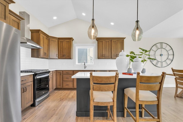 kitchen with appliances with stainless steel finishes, pendant lighting, vaulted ceiling, and wall chimney exhaust hood