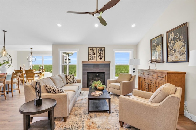 living room with a tile fireplace, light wood-type flooring, ceiling fan, and lofted ceiling