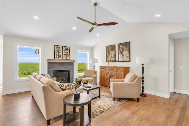 living room with a tile fireplace, light hardwood / wood-style flooring, ceiling fan, and lofted ceiling