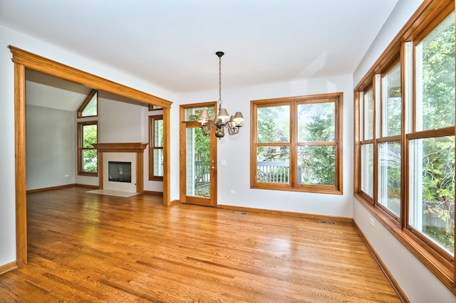 unfurnished living room featuring a chandelier, light hardwood / wood-style floors, vaulted ceiling, and plenty of natural light