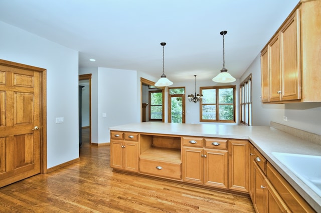 kitchen featuring pendant lighting, sink, kitchen peninsula, a notable chandelier, and light hardwood / wood-style floors