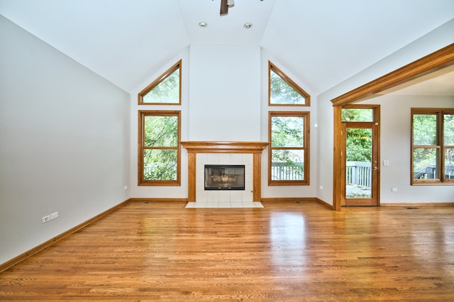 unfurnished living room featuring ceiling fan, a tiled fireplace, light hardwood / wood-style flooring, and high vaulted ceiling