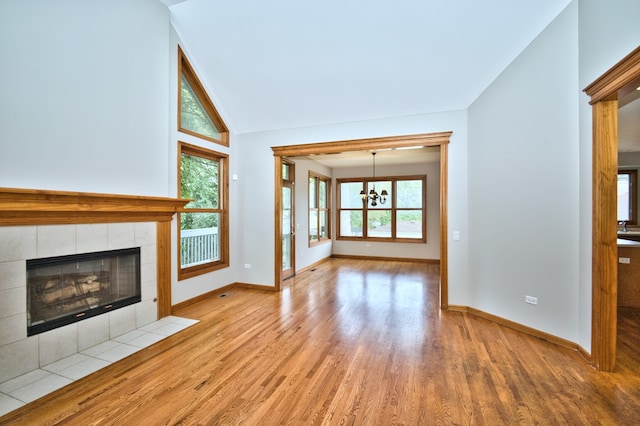 unfurnished living room featuring an inviting chandelier, a fireplace, light hardwood / wood-style floors, and a wealth of natural light