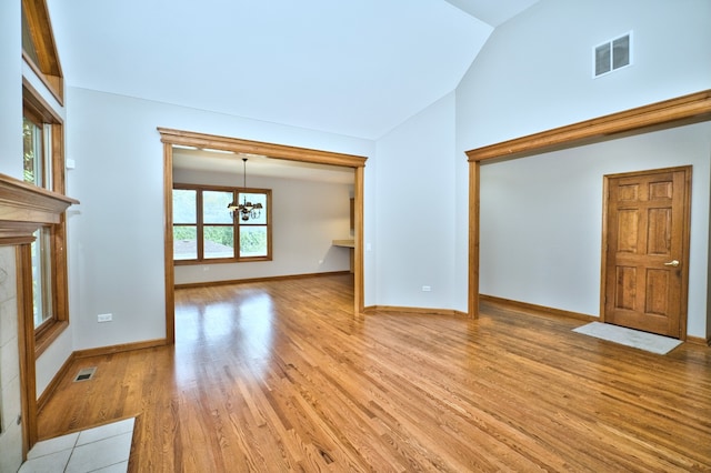 unfurnished living room with an inviting chandelier, light wood-type flooring, and vaulted ceiling