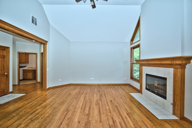 unfurnished living room featuring light hardwood / wood-style flooring, a tiled fireplace, ceiling fan, and high vaulted ceiling