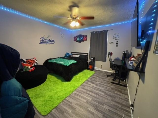 bedroom featuring ceiling fan, golf simulator, hardwood / wood-style floors, and a textured ceiling