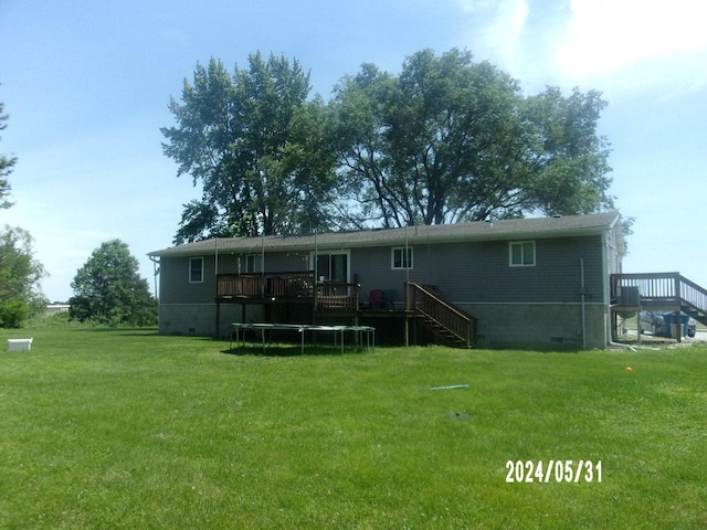 rear view of house featuring a trampoline, a lawn, and a deck