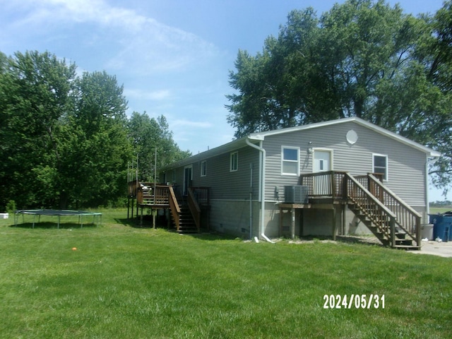 back of property with a trampoline, cooling unit, a yard, and a wooden deck