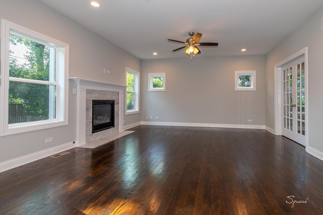 unfurnished living room featuring ceiling fan, a wealth of natural light, a fireplace, and dark wood-type flooring