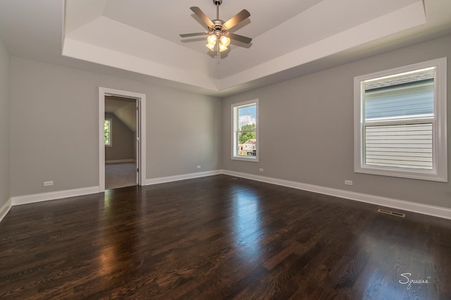 unfurnished room with dark wood-type flooring, a raised ceiling, and a wealth of natural light