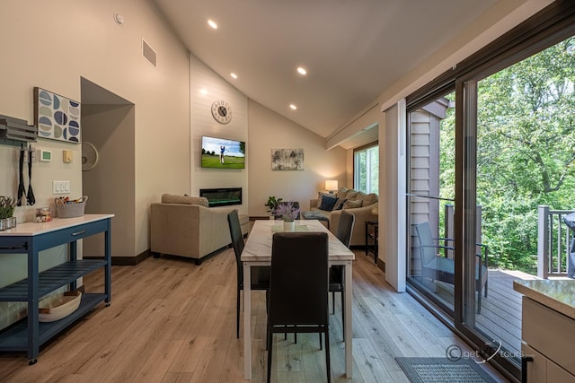 dining room featuring a fireplace, high vaulted ceiling, and light hardwood / wood-style flooring