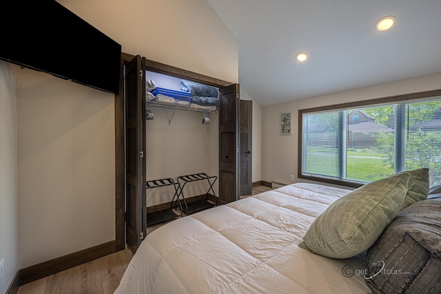 bedroom with hardwood / wood-style floors, lofted ceiling, a baseboard radiator, and a closet