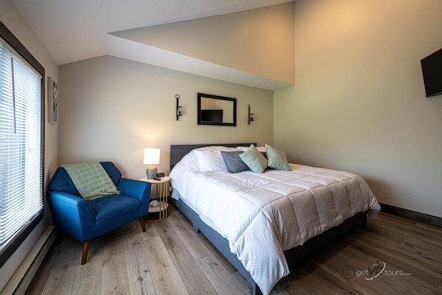 bedroom featuring lofted ceiling, wood-type flooring, and a baseboard heating unit