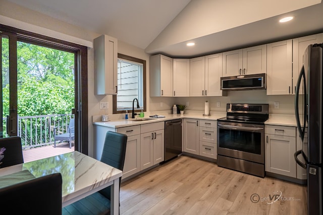 kitchen featuring white cabinetry, sink, stainless steel appliances, light hardwood / wood-style flooring, and vaulted ceiling