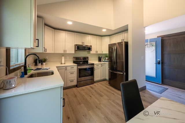 kitchen with appliances with stainless steel finishes, a towering ceiling, sink, light hardwood / wood-style flooring, and white cabinetry