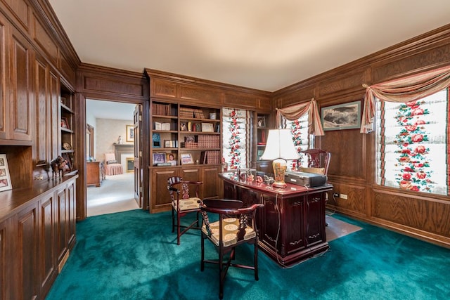 carpeted home office featuring built in shelves, crown molding, and wooden walls