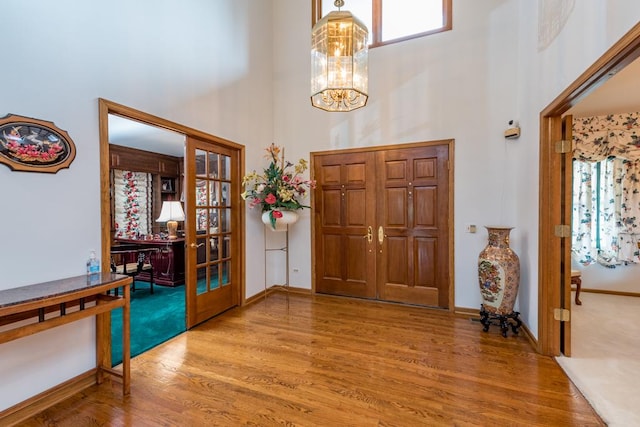 foyer with a notable chandelier, a healthy amount of sunlight, wood-type flooring, and a towering ceiling