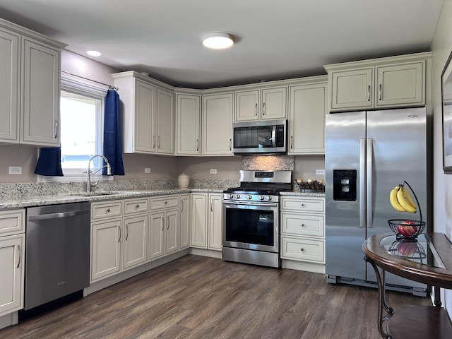 kitchen featuring light stone countertops, appliances with stainless steel finishes, a sink, dark wood finished floors, and recessed lighting