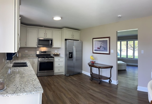 kitchen with dark wood-style flooring, appliances with stainless steel finishes, light stone countertops, a sink, and baseboards