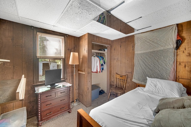 carpeted bedroom with wooden walls, a closet, and a paneled ceiling