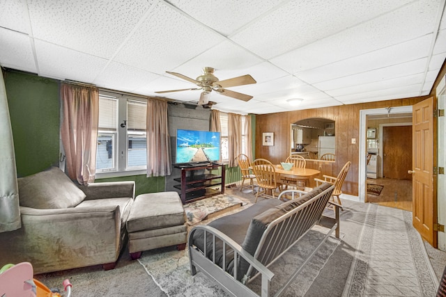 carpeted living room with wooden walls, ceiling fan, and a drop ceiling