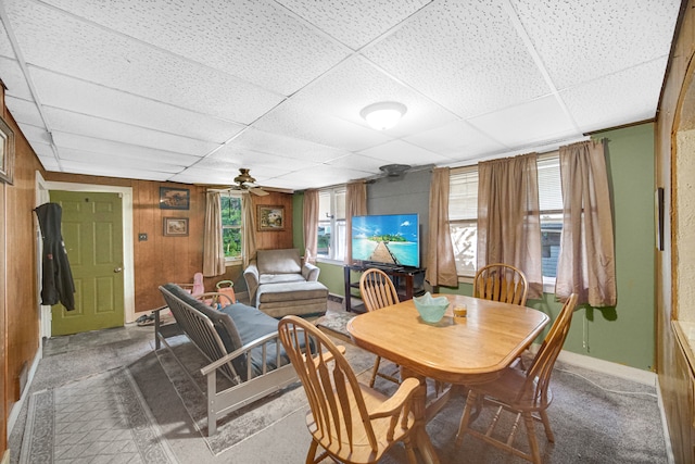 dining space with wooden walls, ceiling fan, and a paneled ceiling