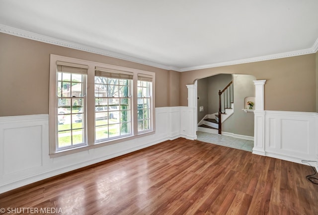 empty room with light hardwood / wood-style flooring, a wealth of natural light, ornamental molding, and ornate columns