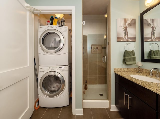 laundry area featuring stacked washer and dryer, dark tile patterned flooring, and sink