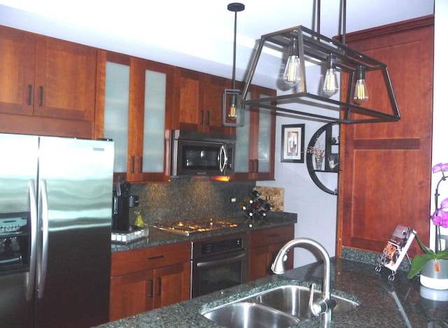 kitchen featuring dark stone counters, sink, appliances with stainless steel finishes, tasteful backsplash, and decorative light fixtures