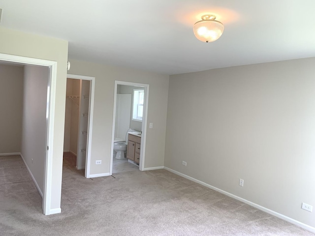 unfurnished bedroom with light carpet, a walk in closet, ensuite bath, and a closet