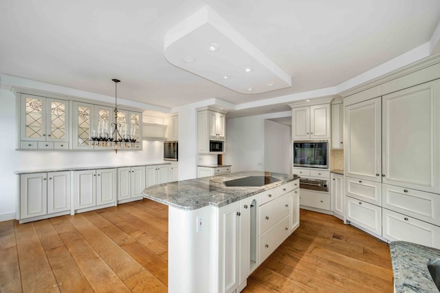 kitchen with light stone counters, light wood-type flooring, a kitchen island, pendant lighting, and black appliances