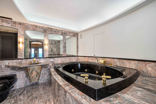 bathroom featuring sink, a tray ceiling, and tiled bath