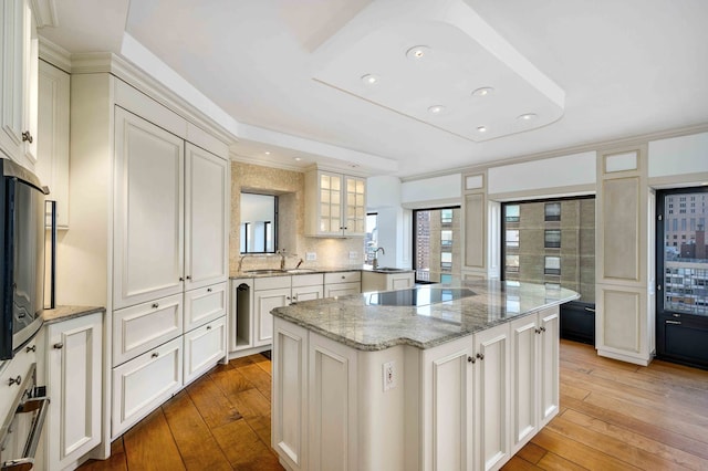 kitchen with a kitchen island, white cabinets, black electric stovetop, light stone countertops, and light hardwood / wood-style flooring