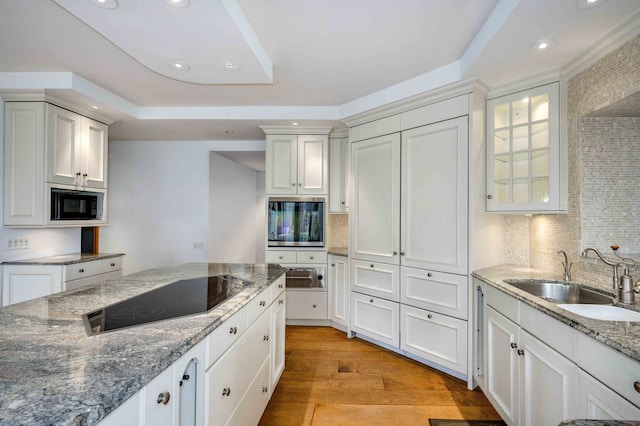 kitchen featuring tasteful backsplash, sink, white cabinets, light hardwood / wood-style floors, and black appliances