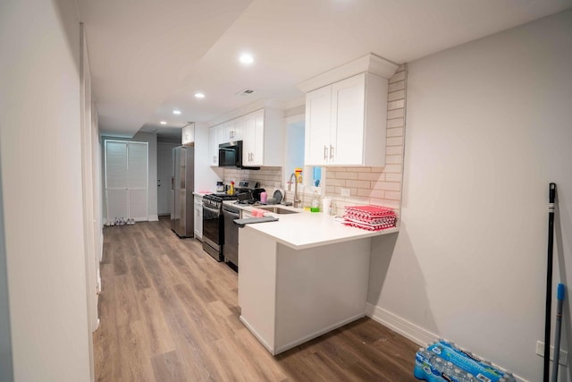 kitchen featuring kitchen peninsula, light wood-type flooring, stainless steel appliances, sink, and white cabinets