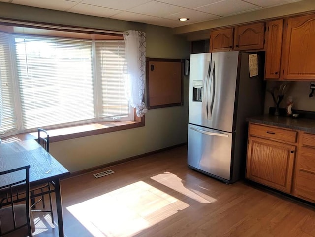 kitchen with stainless steel refrigerator with ice dispenser, a drop ceiling, light hardwood / wood-style flooring, and plenty of natural light