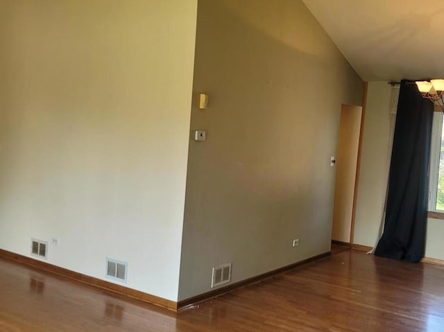 empty room featuring a chandelier, dark hardwood / wood-style flooring, and vaulted ceiling