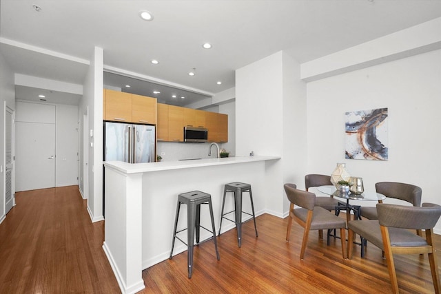 kitchen with sink, light brown cabinets, kitchen peninsula, hardwood / wood-style floors, and appliances with stainless steel finishes