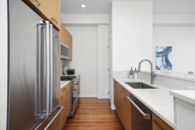 kitchen featuring light stone countertops, dark hardwood / wood-style flooring, premium appliances, and sink