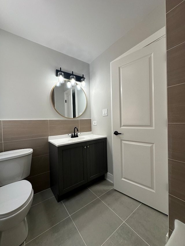 bathroom with toilet, vanity, tile patterned floors, and tile walls