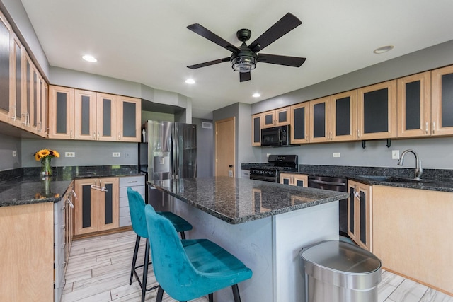 kitchen with a breakfast bar, a center island, black appliances, sink, and ceiling fan