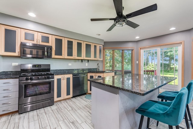 kitchen with a kitchen bar, stainless steel appliances, ceiling fan, sink, and a center island