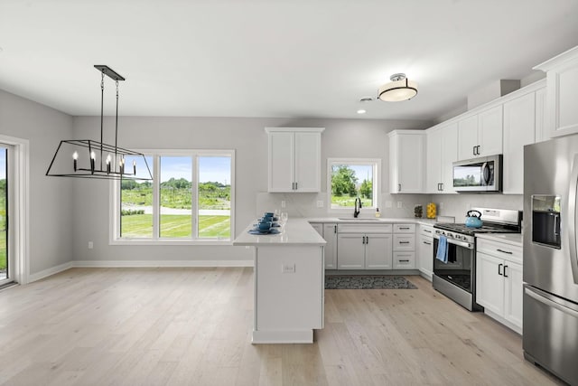 kitchen featuring appliances with stainless steel finishes, a sink, light countertops, a peninsula, and white cabinetry