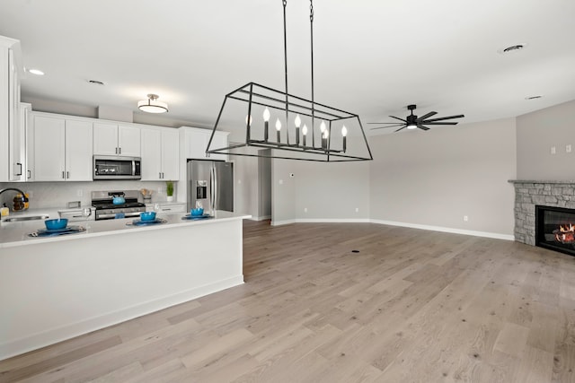 kitchen featuring stainless steel appliances, light wood-type flooring, hanging light fixtures, sink, and white cabinets