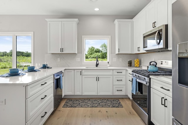 kitchen with appliances with stainless steel finishes, a sink, a peninsula, light wood finished floors, and recessed lighting