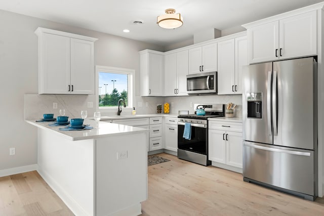 kitchen with backsplash, appliances with stainless steel finishes, light hardwood / wood-style flooring, and white cabinets