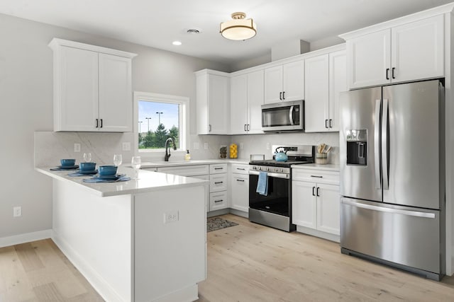 kitchen featuring a peninsula, light countertops, a sink, light wood-style flooring, and appliances with stainless steel finishes